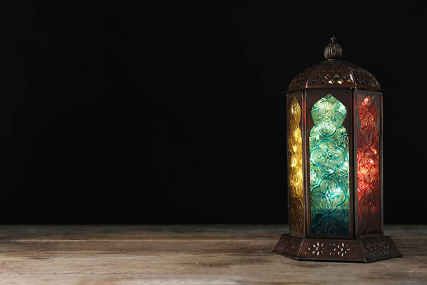Decorative Arabic lantern on wooden table against black background, space for text - Photo, Image