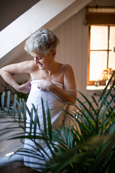 Happy senior woman wrapped in a towel in bathroom at home. - Foto, Imagen