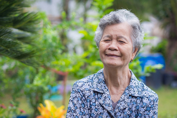 Portrait d'une femme âgée souriante et regardant la caméra debout dans un jardin. Espace pour le texte. Concept de personnes âgées et soins de santé - Photo, image