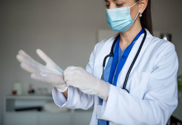 Portrait of woman doctor putting on gloves in hospital, coronavirus concept. - Φωτογραφία, εικόνα