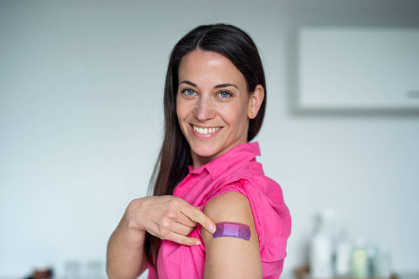 Mujer feliz con yeso en el brazo después de la vacunación en el hospital, mirando a la cámara. - Foto, Imagen