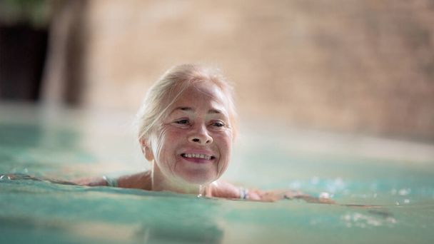 Portrait of senior woman in indoor swimming pool, swimming. - Фото, изображение