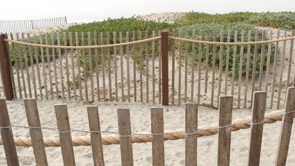 Wooden picket fence, sandy misty beach, California USA. Pacific ocean coast, fog haze on sea shore. - Photo, Image