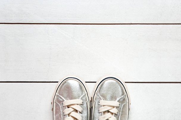 kind metalen zilveren sneakers op witte houten plank achtergrond textuur met kopieerruimte. Witte sneakers voor meisjes. Bovenaanzicht - Foto, afbeelding
