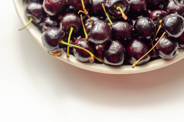 Close-up em cerejas doces frescas e maduras em uma placa de cerâmica branca, frutas suculentas - Foto, Imagem
