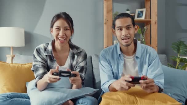 Šťastný asijské mladý pár muž a žena sedět na gauči pomocí joystick regulátor hrát videohry strávit zábavný čas spolu v obývacím pokoji. Asijské ženatý pár rodinný životní styl, pár pobyt doma koncept. - Záběry, video