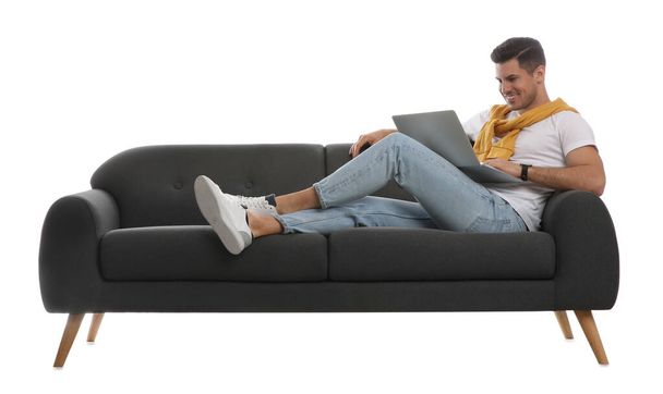 Man with laptop on comfortable grey sofa against white background - Foto, afbeelding