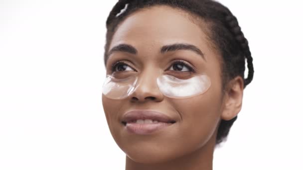 Beauty portrait of young african american lady with cooling hydrogel patches under eyes area, white studio background - Footage, Video