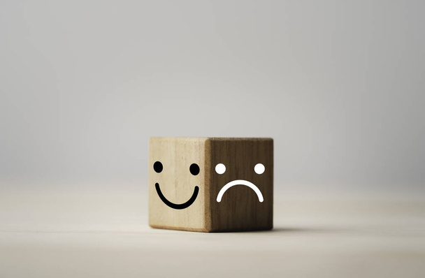 Faccia sorridente sul lato luminoso e tristezza sul lato oscuro del blocco cubo in legno, selezione delle emozioni e concetto di mentalità. - Foto, immagini