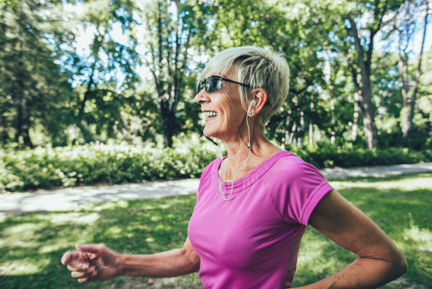Mulher idosa correndo com fones de ouvido no parque - Foto, Imagem