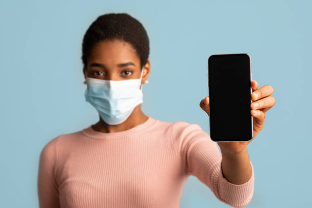 Mladá africká žena v lékařské masce ukazující smartphone s prázdnou černou obrazovkou - Fotografie, Obrázek