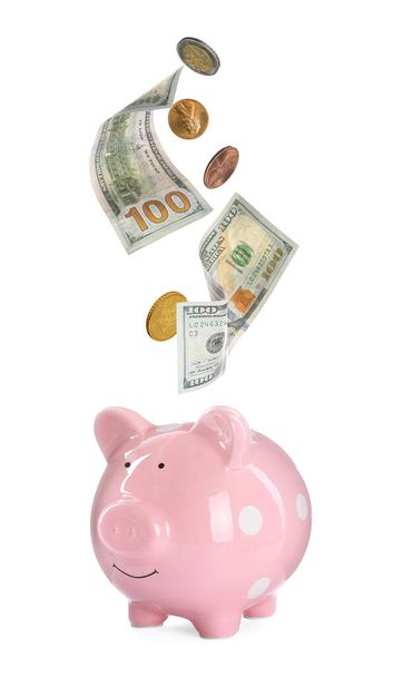 Banknotes and coins falling into piggy bank on white background. Saving money - Foto, afbeelding
