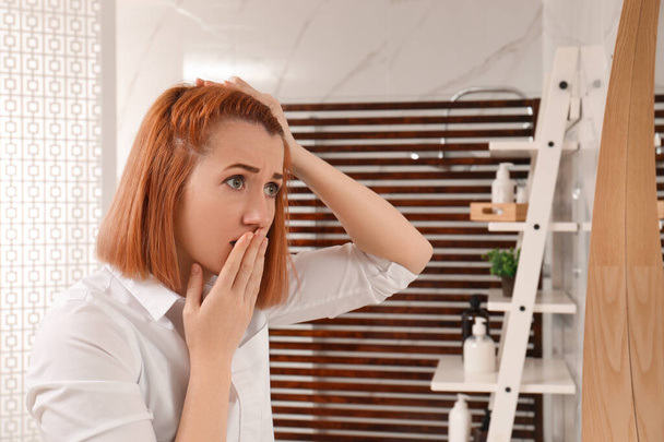 Emotional woman suffering from baldness near mirror at home - Foto, imagen