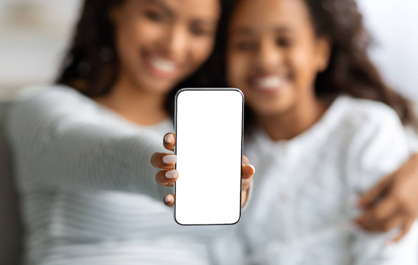 Zwarte moeder en dochter tonen smartphone met leeg scherm - Foto, afbeelding