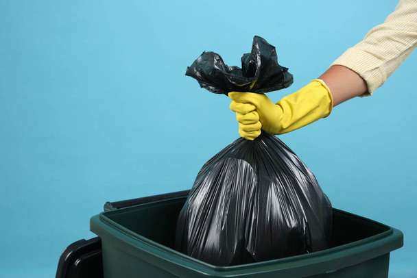 Woman throwing garbage bag into bin on light blue background, closeup - Fotografie, Obrázek