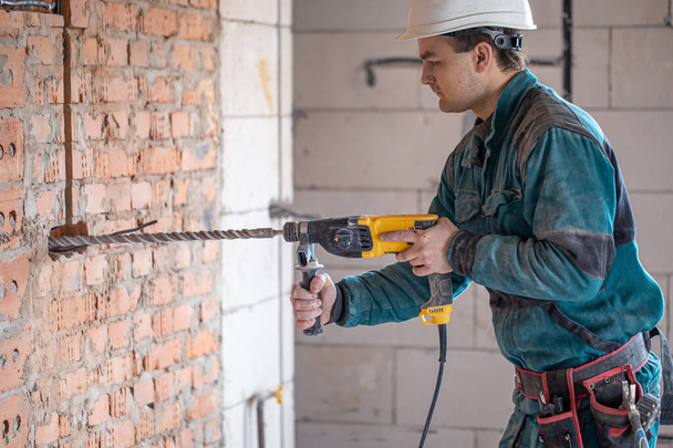 Handyman no processo de perfuração de uma parede com um perfurador. - Foto, Imagem