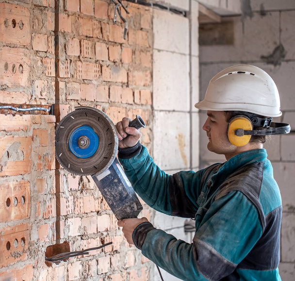 Ein professioneller Bauarbeiter in Arbeitskleidung arbeitet mit einem Schneidwerkzeug. - Foto, Bild