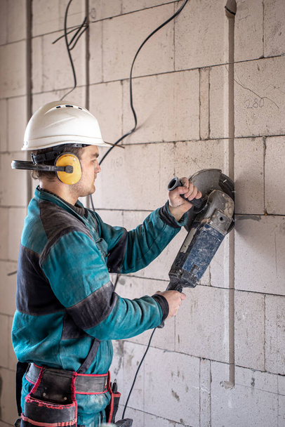 Ein professioneller Bauarbeiter in Arbeitskleidung arbeitet mit einem Schneidwerkzeug. - Foto, Bild