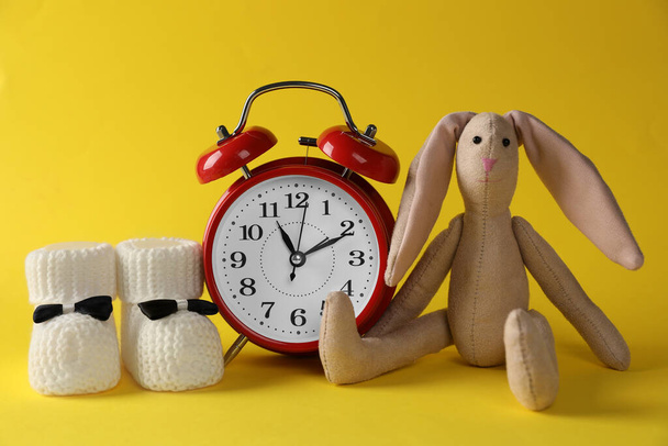 Alarm clock, bunny and baby booties on yellow background. Time to give birth - Fotó, kép