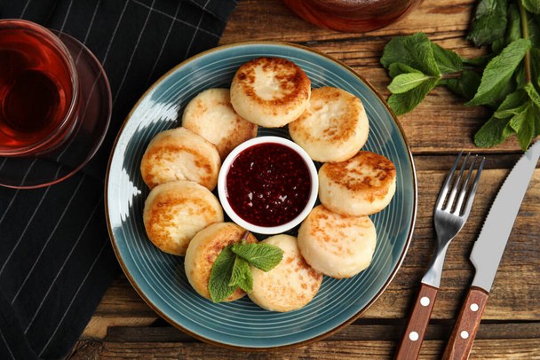 Delicious cottage cheese pancakes with jam and mint on wooden table, flat lay - 写真・画像