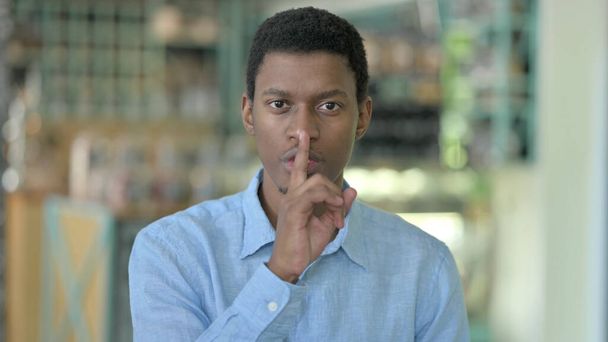 Porträt eines jungen Afrikaners, der den Finger auf die Lippen legt  - Foto, Bild