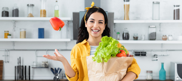 happy brunette woman throwing in air bell peppers and holding paper bag with groceries, banner - Foto, Bild