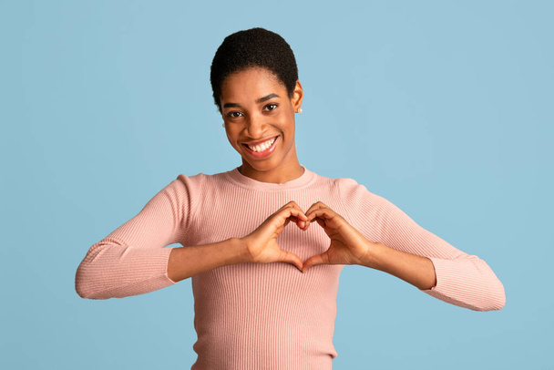 Pozytywna afrykańska kobieta wykazująca gest serca dłońmi w pobliżu klatki piersiowej - Zdjęcie, obraz