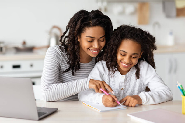 Красива чорна мати допомагає доньці з домашнім завданням
 - Фото, зображення