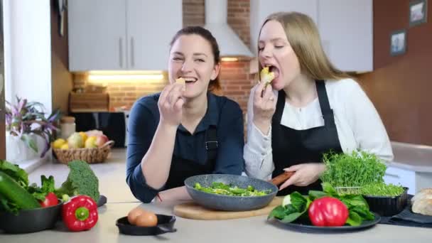 koncepcja doświadczeń żywieniowych w domowej kuchni i w domowej kuchni. Kobiety w czarnych fartuchach jedzące gotowany posiłek w kuchni - Materiał filmowy, wideo