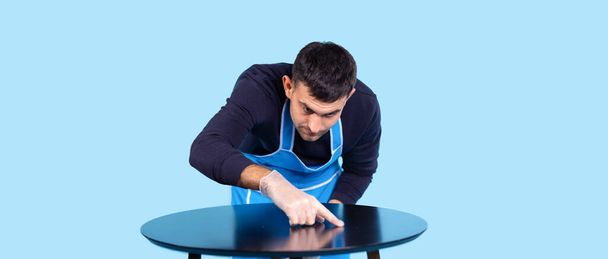 Banner, long format, blue background. Male hand in protective gloves checking dust on surface table. Concentrated man holding forefinger on clean glass. General cleaning at home. High quality photo - Foto, afbeelding