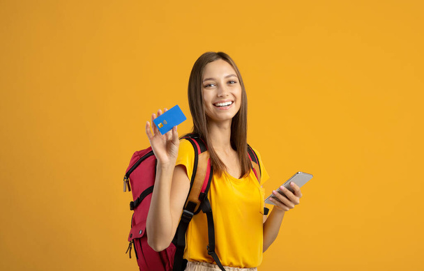 Happy woman backpacker with smartphone and credit card on yellow - Foto, Imagem
