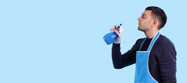 Banner, long format isolated blue background. Funny cleaning time. Profile view of playful man holds cleaning spray in hand like a gun and blows off gunpowder as after a shot. . High quality photo - Valokuva, kuva