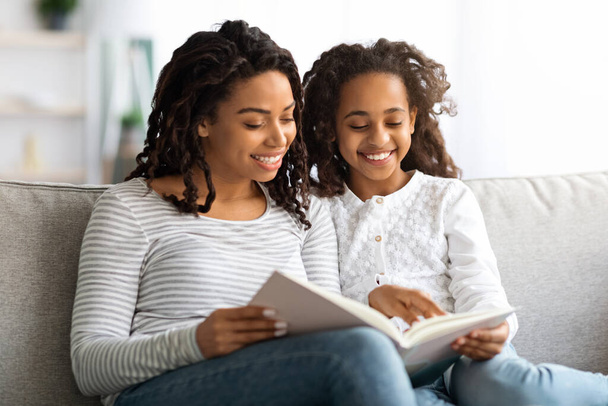 Χαρούμενη μαύρη μητέρα και κόρη διαβάζουν μαζί το βιβλίο. - Φωτογραφία, εικόνα