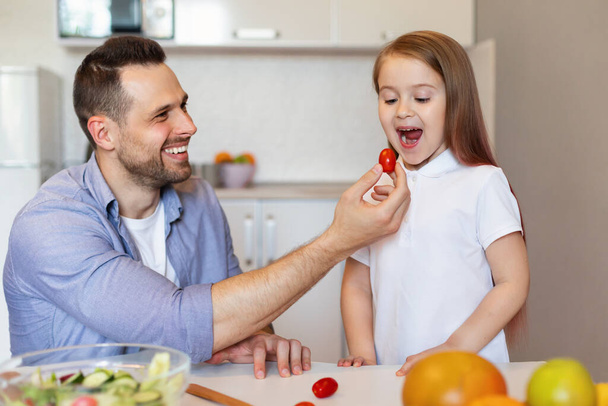 Радісний татко годує доньку веселим куховарством на кухні - Фото, зображення