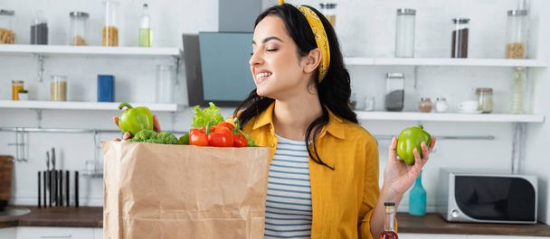 happy brunette woman looking at paper bag with fresh groceries, banner - Photo, image