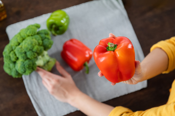 cropped view of woman holding red bell pepper near vegetables on blurred background  - Photo, Image