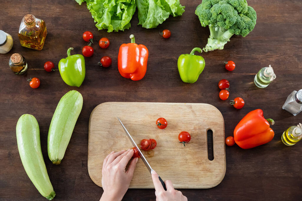 top view of woman cutting cherry tomatoes on chopping board near vegetables  - Photo, Image