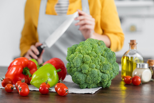 спелые овощи рядом с женщиной с ножом на размытом фоне  - Фото, изображение