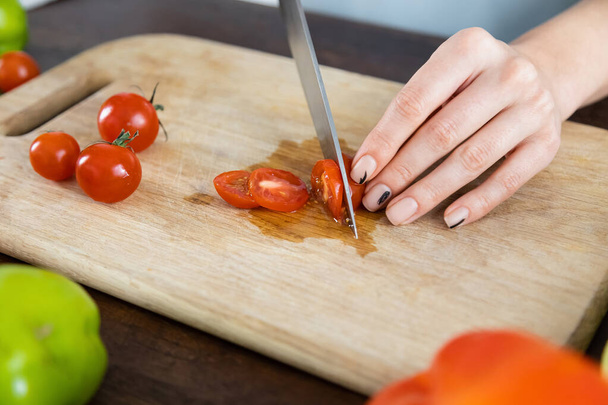cropped view of woman cutting red cherry tomatoes on wooden chopping board  - Fotoğraf, Görsel