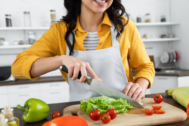 cropped view of smiling woman cutting fresh lettuce near cherry tomatoes on wooden chopping board  - Foto, immagini
