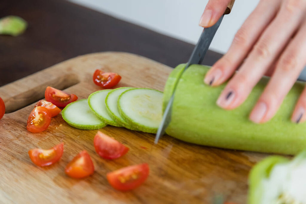 vista recortada de la mujer cortando calabacín cerca de tomates cherry en la tabla de cortar  - Foto, Imagen