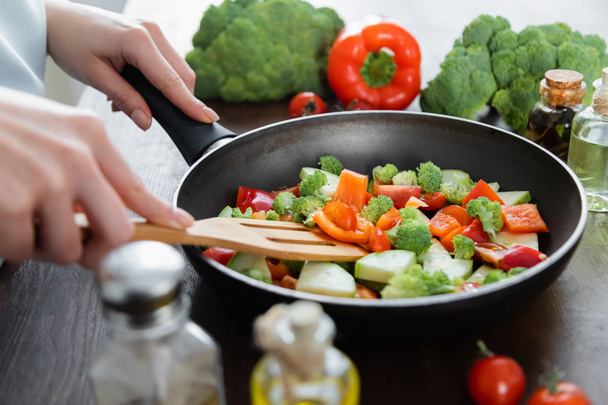 partial view of woman mixing sliced vegetables on frying pan with spatula  - Photo, Image