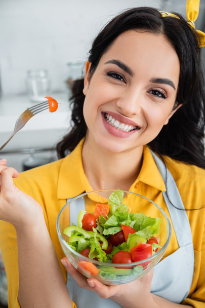cheerful young woman holding fork with cherry tomato near salad in bowl - Foto, Imagem
