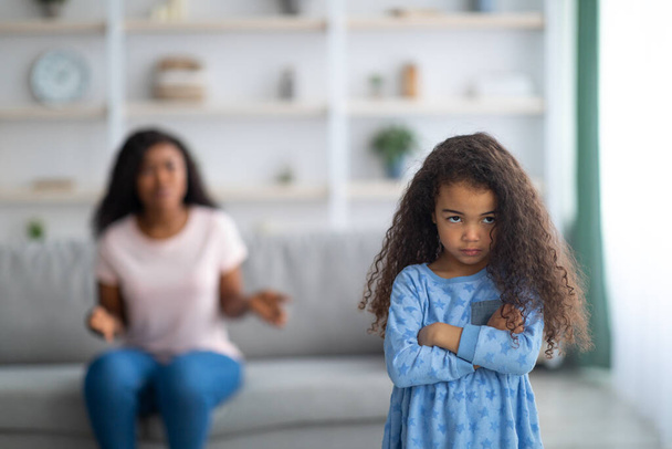 Little black girl feeling unhappy and offended, being scolded by her angry tired mother at home, blank space - Фото, изображение