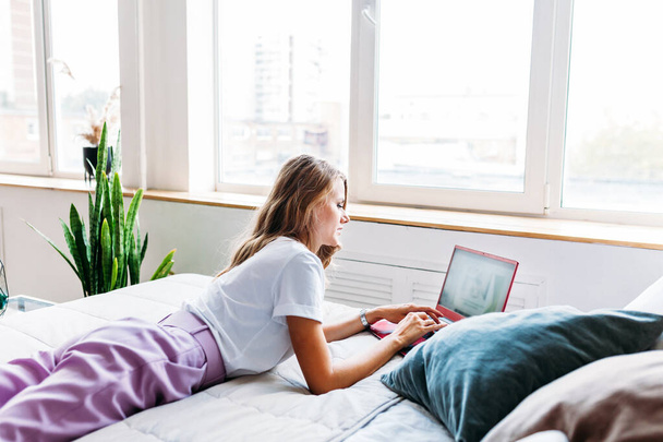 Girl lying on bed with working on laptop, entertainment, remote work, freelance, home office - Foto, Bild