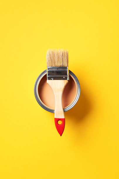 Brush and open paint can with on trendy yellow background. Top view, copy space. Appartment renovation, repair, building and home design concept. - Photo, Image