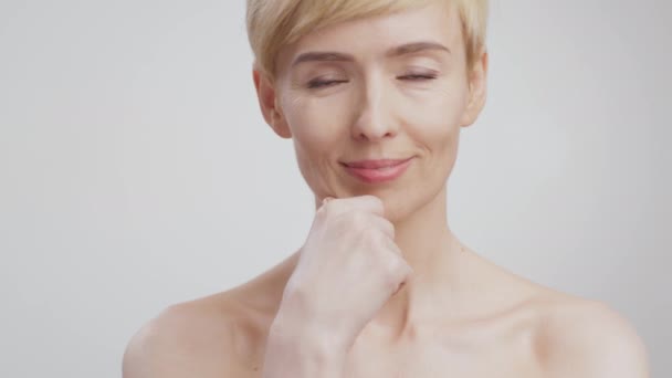 Portrait of gorgeous middle aged lady touching her perfect face skin, smiling to camera, grey studio background - Footage, Video