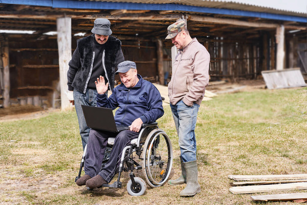 Счастливый старший мужчина в повседневной одежде в инвалидной коляске во дворе своего дома с друзьями - Фото, изображение