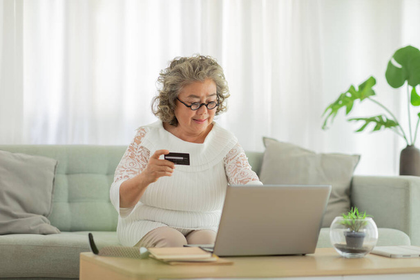 Happiness of wellness elderly asian woman with white hairs sitting on sofa using computer laptop and using credit card to shopping online and payment at home,Senior lifestyle at home concept - Foto, Bild