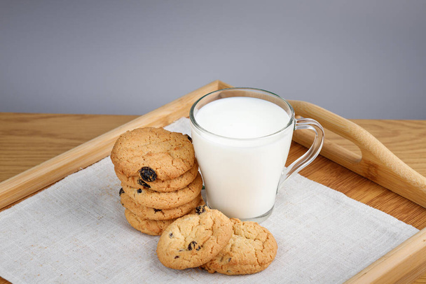 Copo de leite e biscoitos com passas em uma bandeja de madeira - Foto, Imagem